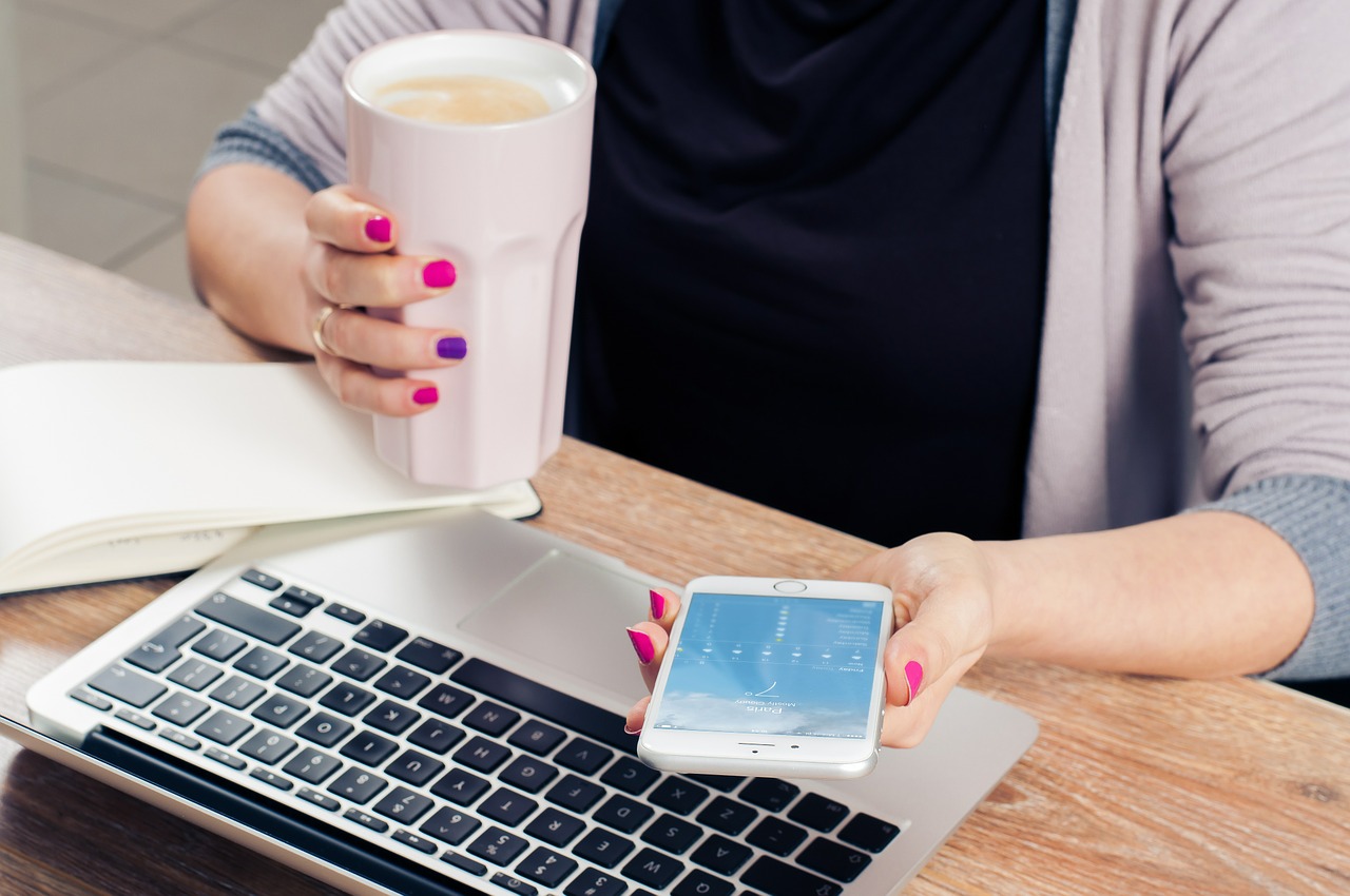 using a smartphone next to a laptop while having a coffee